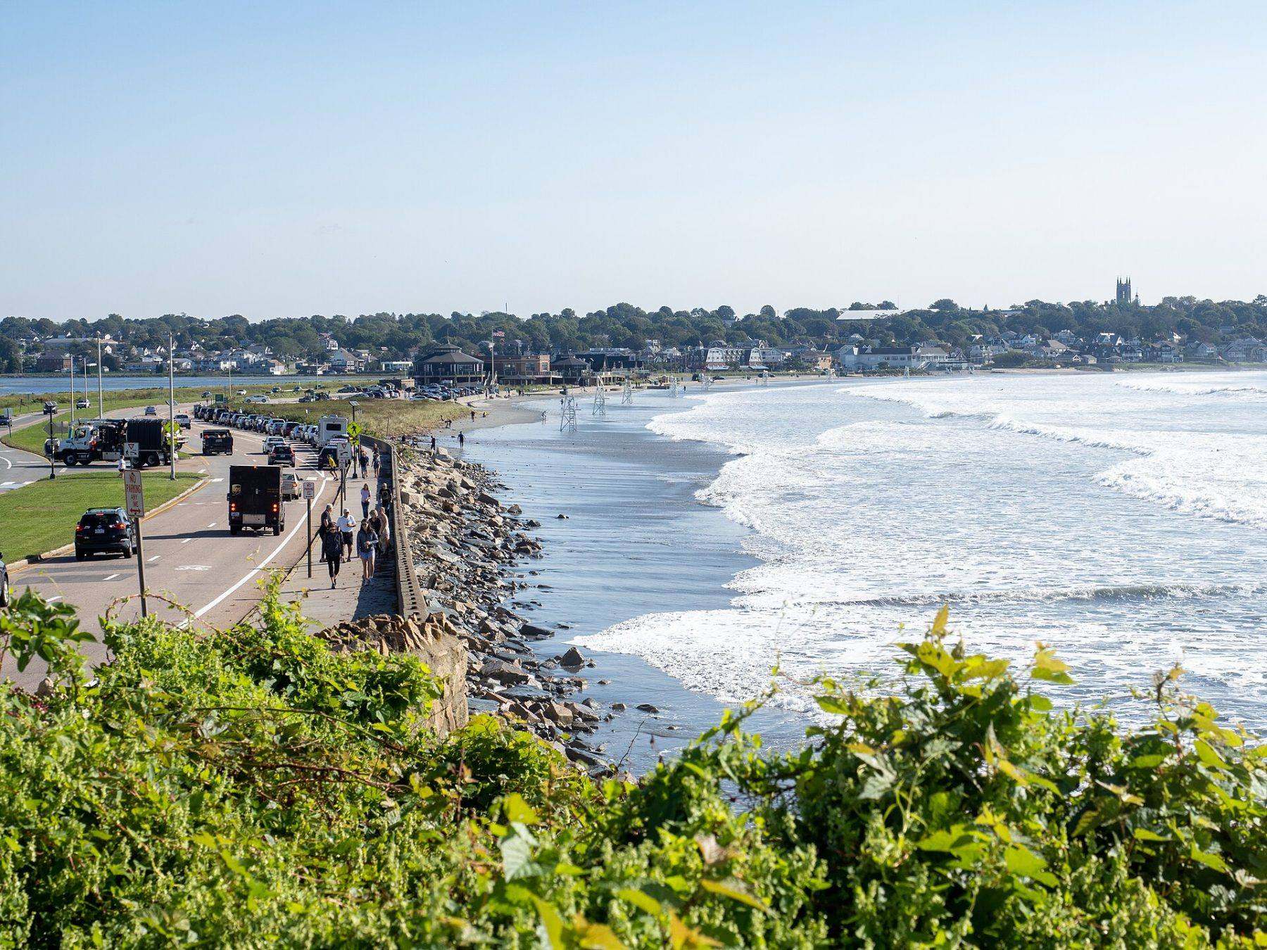 Surf rolling into Easton's Beach in Newport, with the neighborhood behind the seawall